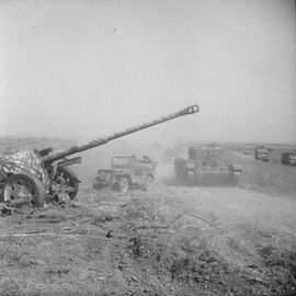 Een Cromwell tank en een Jeep passeren een achtergelaten 88 mm antitankkanon